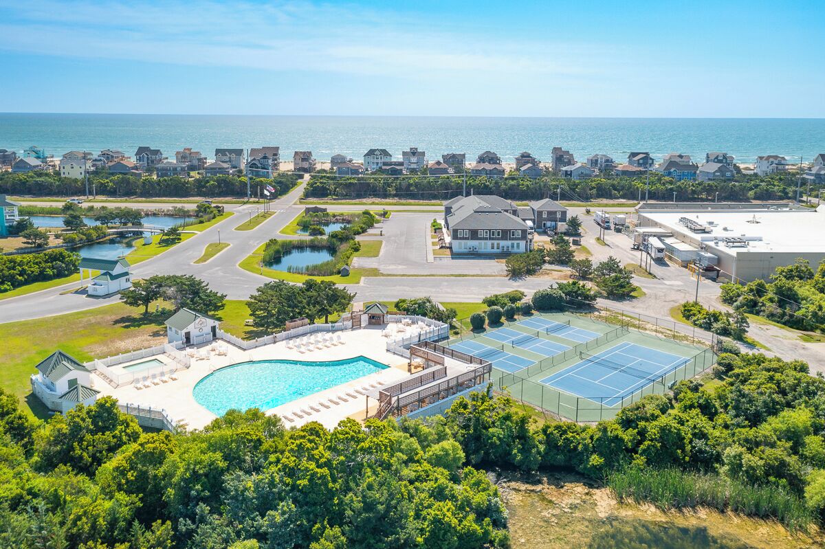 Un quartier résidentiel doté d’une piscine, de courts de tennis et d’une grande maison avec un garage.