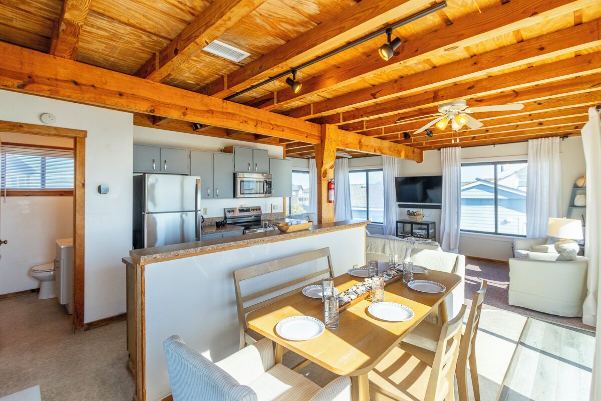 Un'ampia cucina con elettrodomestici moderni, un'area pranzo con tavolo e sedie in legno, e un soggiorno con divano e televisore.