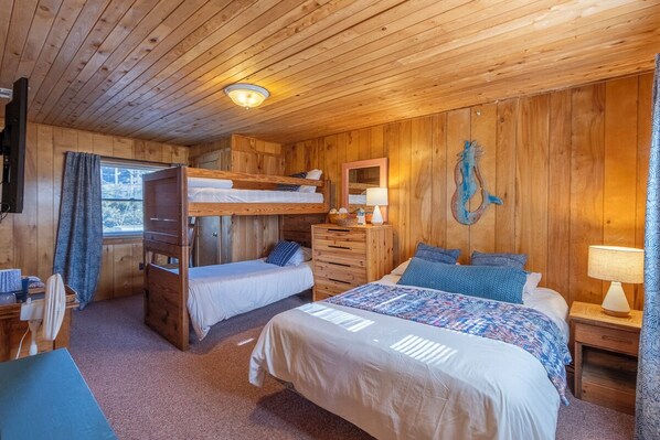Una habitación de cabaña de madera con literas, un escritorio, un aparador y un espejo.
