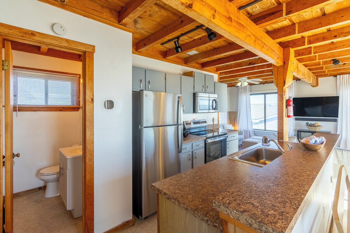 Una cocina compacta con encimera de granito, electrodomésticos de acero inoxidable y techo de madera.