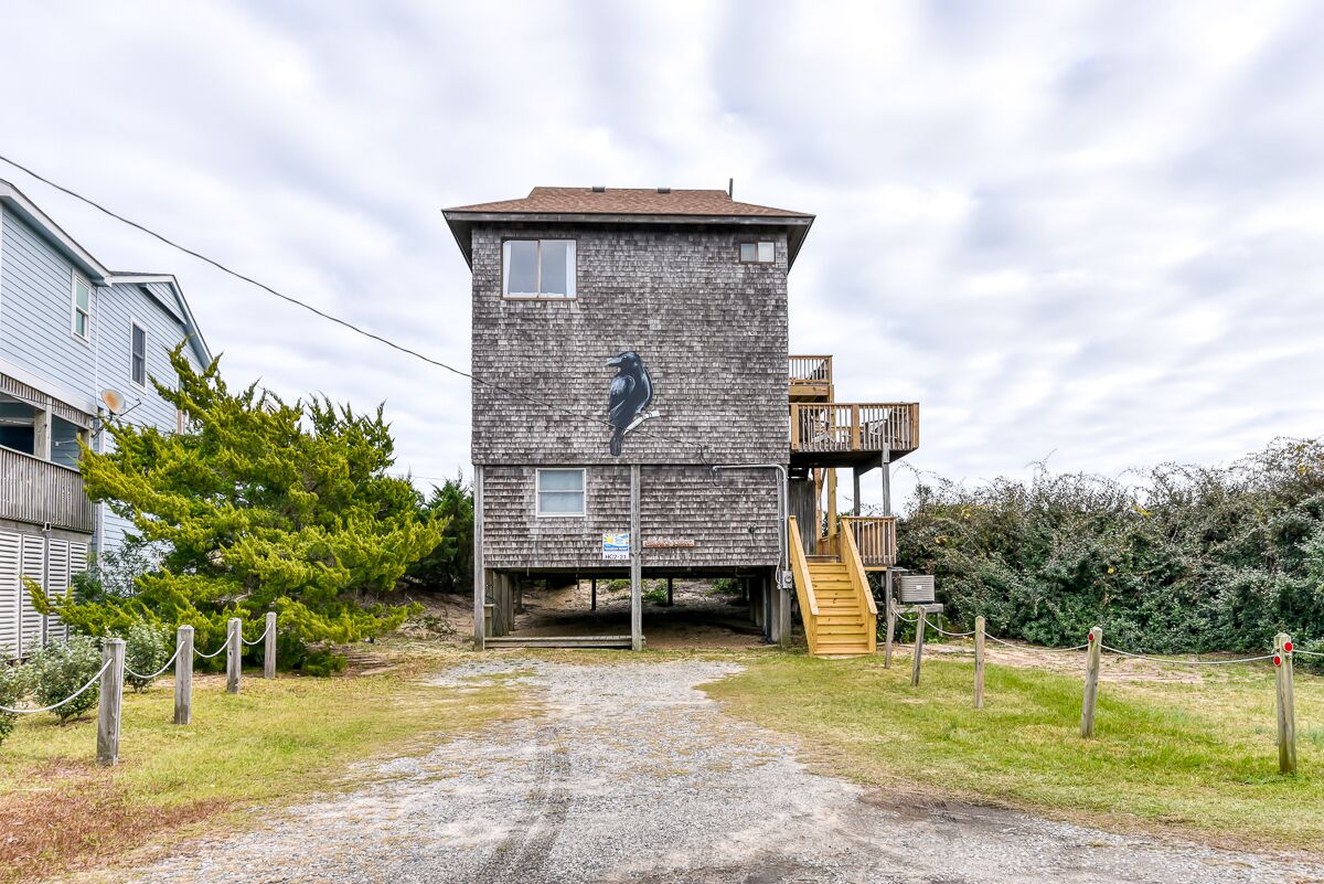 A rustic wooden tower with a staircase leading to a deck, surrounded by a gravel path and greenery.