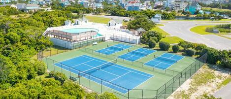 A tennis court surrounded by lush greenery and residential buildings.