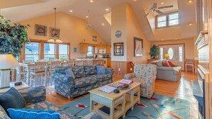 A spacious living area with a high ceiling, multiple seating options, and a kitchen in the background. - Pet friendly Hatteras Island home with private pool, hot tub, and sound views (Avon)