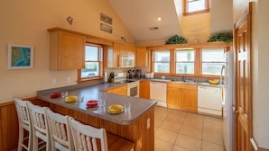 A kitchen with wooden cabinets, a central island, and a view to the outside. - Pet friendly Hatteras Island home with private pool, hot tub, and sound views (Avon)
