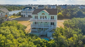 A multi-story house with a balcony and a pool, surrounded by greenery and other houses. - Pet friendly Hatteras Island home with private pool, hot tub, and sound views (Avon)