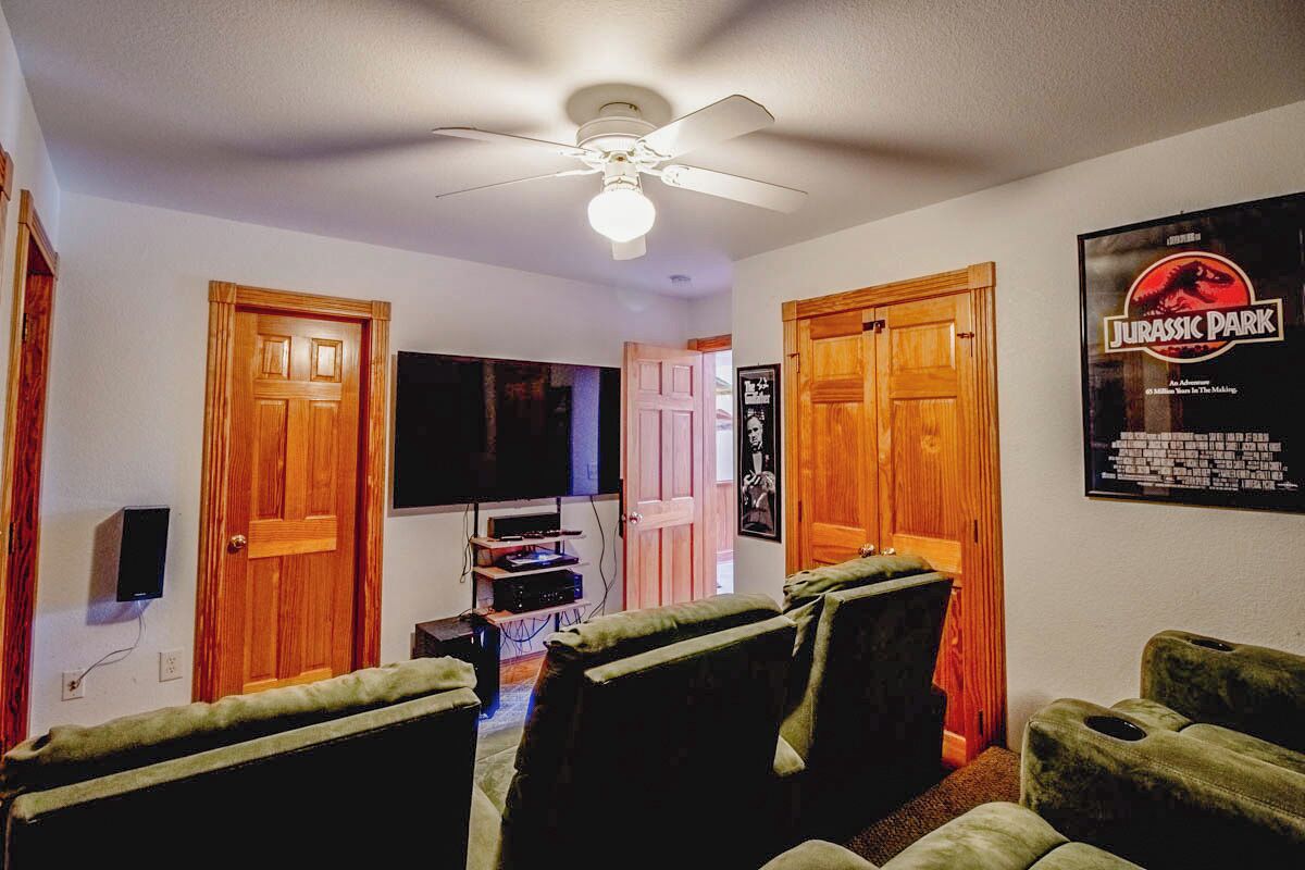 A living room with a ceiling fan, wooden doors, a flat-screen TV, and a poster of Jurassic Park.