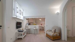Een moderne, compacte leefruimte met een keukenhoek, een eettafel en een zithoek met een bank en stoelen.