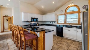 Una cocina con armarios blancos, una isla central, taburetes de bar, un microondas y un refrigerador.