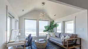 Una sala moderna con un escritorio de cristal, un sofá, una planta grande y vista al océano.
