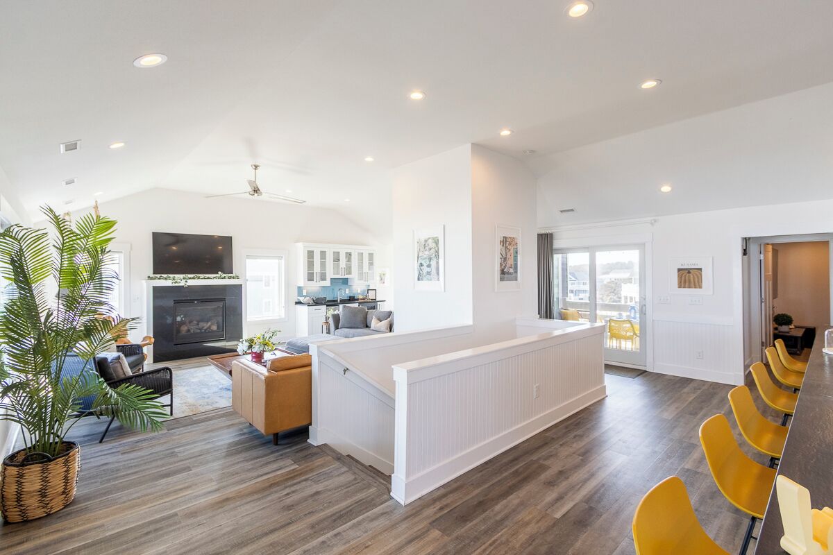 A spacious living area with a fireplace, a dining area with yellow chairs, and a kitchen in the background.