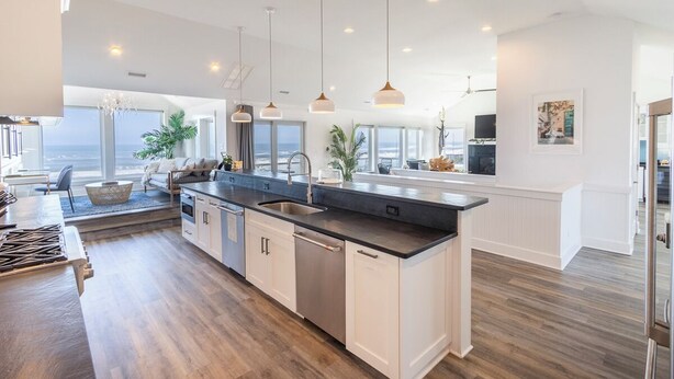 Una cocina moderna con una isla central, iluminación colgante y vistas al océano.