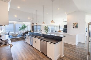Een moderne keuken met een centraal kookeiland, hanglampen en uitzicht op zee.