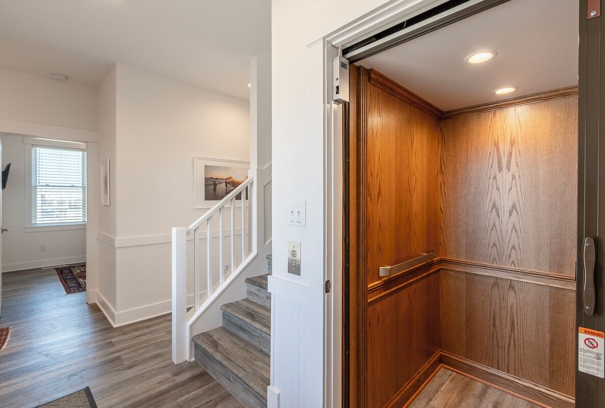 A modern interior with a wooden elevator door, a staircase with white railings, and a view of a balcony through a window.