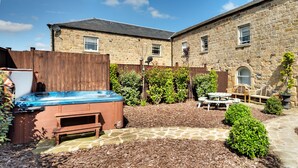 A stone building with a wooden deck, a hot tub, and picnic tables. - The Milking Parlour Grande -9 bedroom property with hot tub (Oakerthorpe)