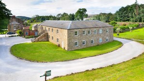 A stone building with a central staircase, surrounded by a well-maintained lawn and a curved driveway. - The Old Milking Parlour - 6 bedroom property with hot tub (Oakerthorpe)