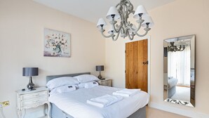 Ein Schlafzimmer mit einem Bett, Nachttischen, einer Kandelaber, einer Holztür und einem Spiegel.