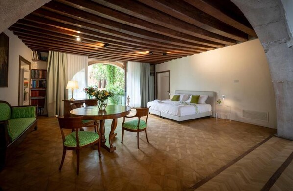 A cozy room with a wooden ceiling, a round dining table with chairs, a bed with pillows, and a bookshelf. - Mocenigo Grand Canal Luxury Suites (Venice)