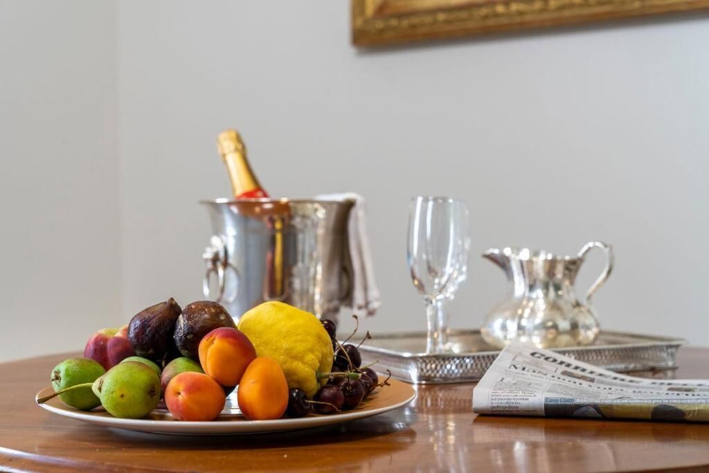 A table with a plate of fruit, a champagne bottle, a glass, and a newspaper.