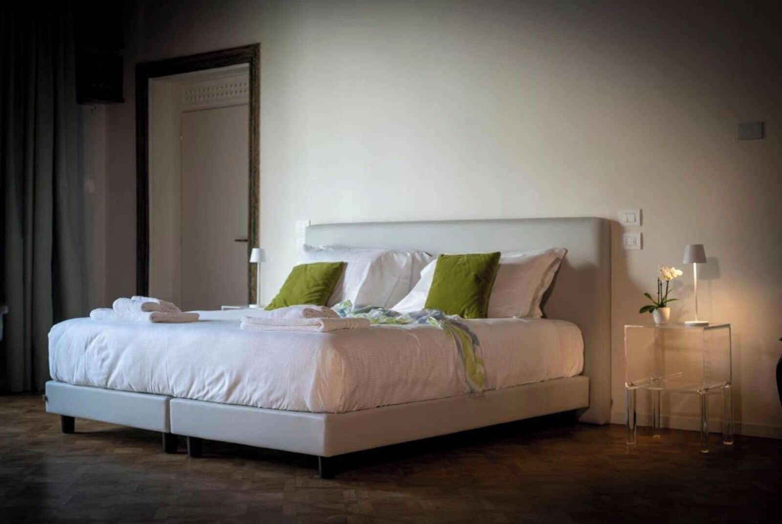 Una habitación de hotel moderna con una cama grande, una mesita de noche con lámpara y una puerta con cerradura electrónica.