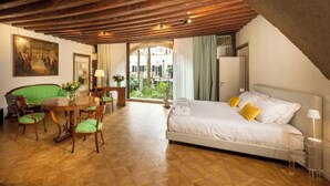 A bedroom with a bed, a dining table with chairs, and a view of greenery outside. - Mocenigo Grand Canal Luxury Suites (Venice)