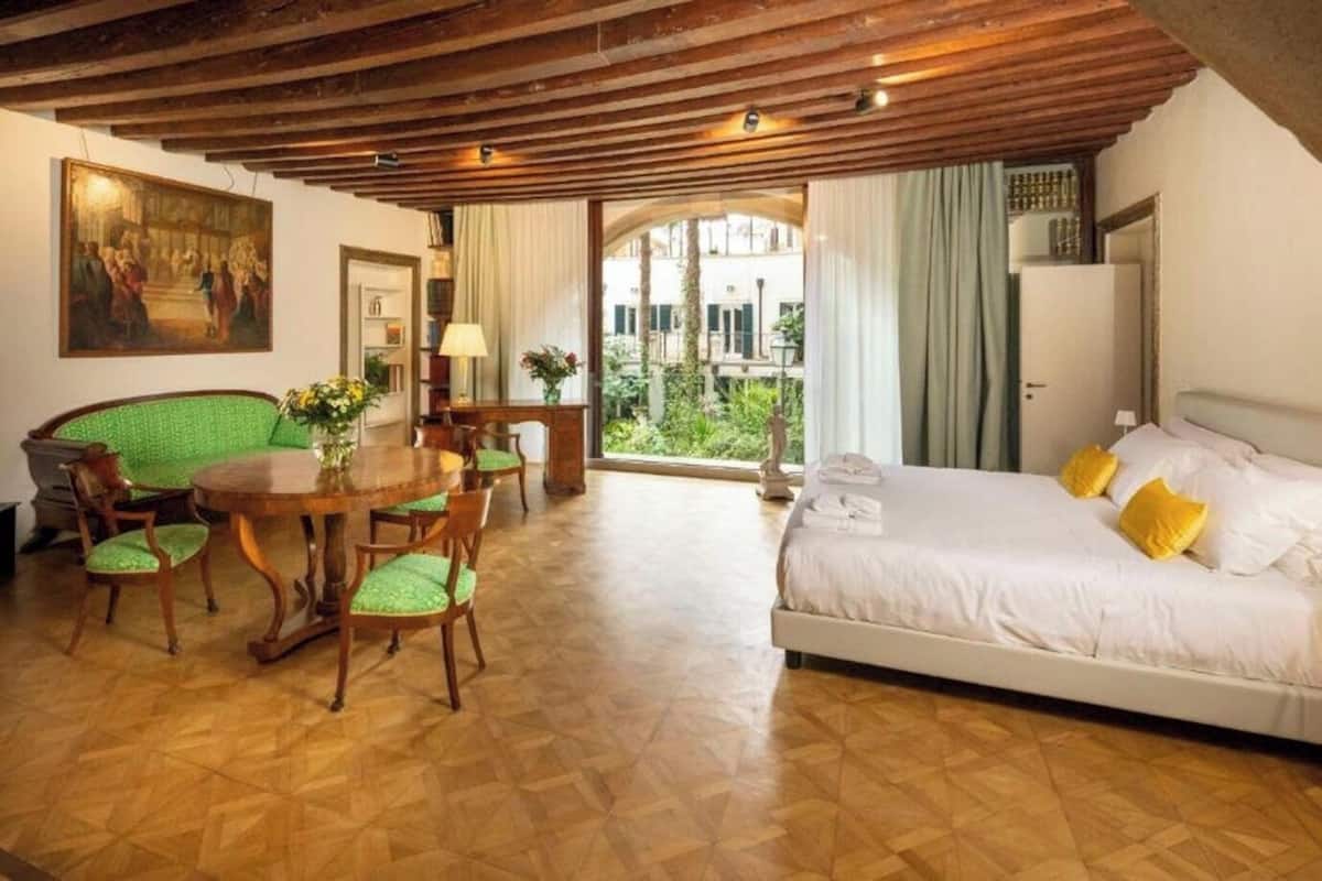 Un dormitorio con cama, una mesa de comedor con sillas y vista a zonas verdes.