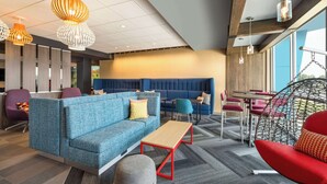 Un moderno espacio lounge con diferentes disposiciones de asientos, incluyendo un sofá azul, sillas rojas y una silla colgante.