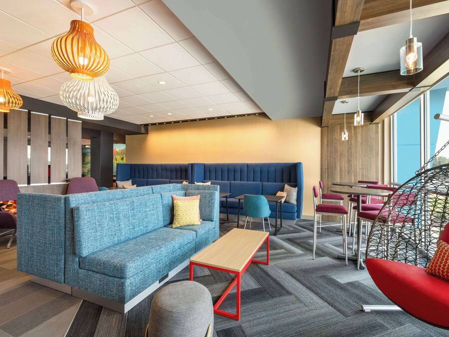 A modern lounge area with seating arrangements, including a blue sofa, red chairs, and a hanging chair.