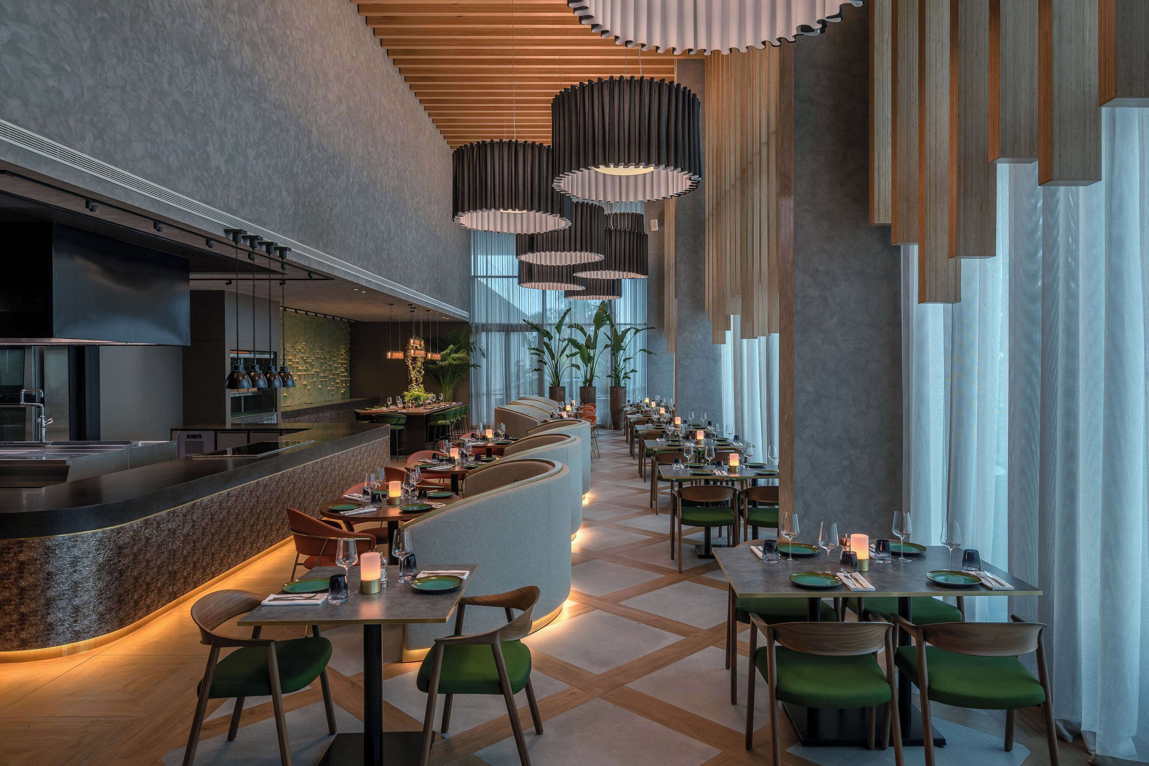 Een modern restaurant met een lange toonbank, meerdere eettafels en groene stoelen.
