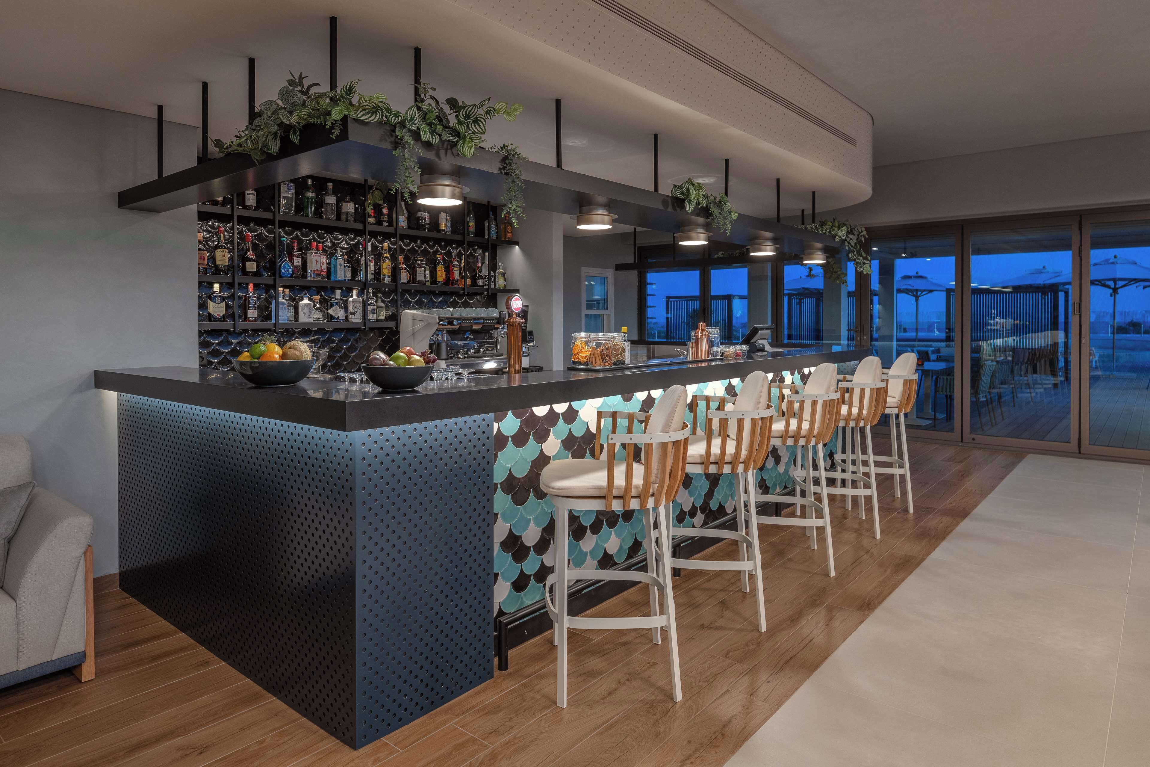 A modern bar area with a long counter, bar stools, and a variety of bottles.