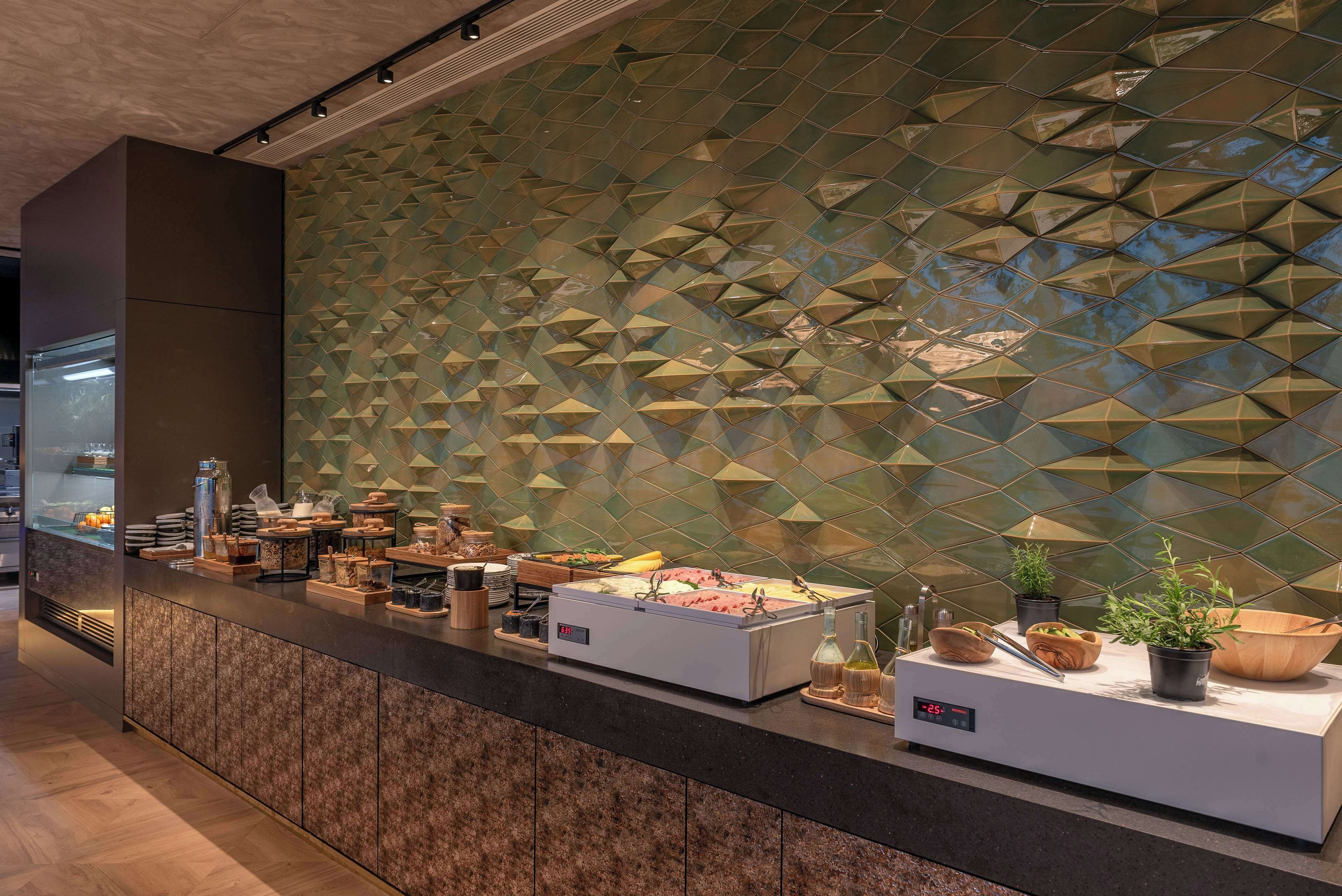 A buffet area with a geometric patterned wall, a variety of food items, and a digital temperature display.