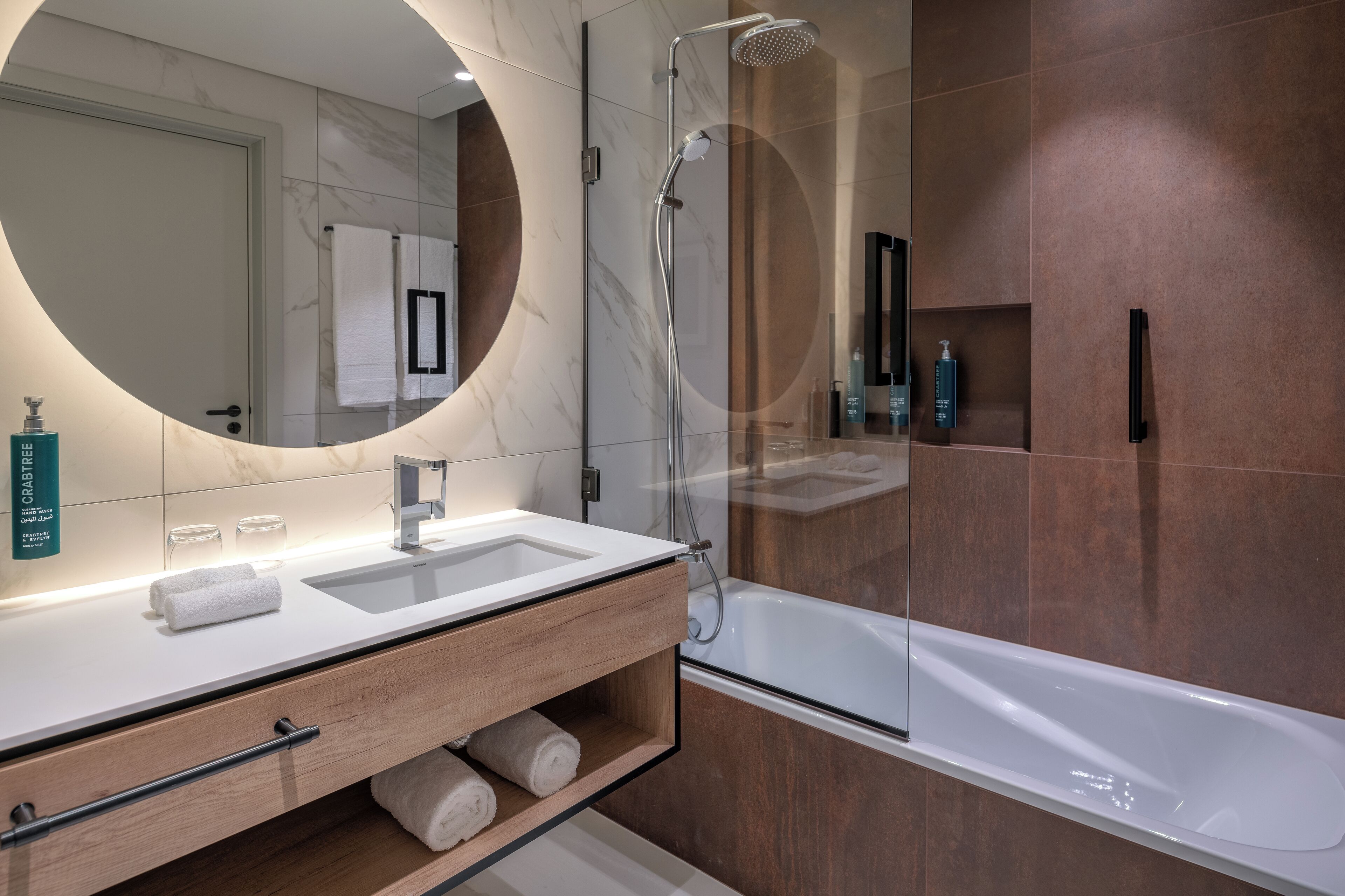A modern bathroom with a large mirror, a white sink, a wooden vanity, and a glass-enclosed shower.