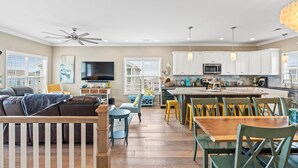 A modern kitchen with white cabinets, a central island, and a dining area with yellow chairs. - Rainbow Skies- 5 bedroom, 4 bath w/private pool, OIB resort & steps to the beach (Ocean Isle Beach)