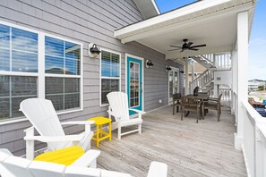 A covered deck with Adirondack chairs, a table, and a staircase leading to a second level. - Rainbow Skies- 5 bedroom, 4 bath w/private pool, OIB resort & steps to the beach (Ocean Isle Beach)