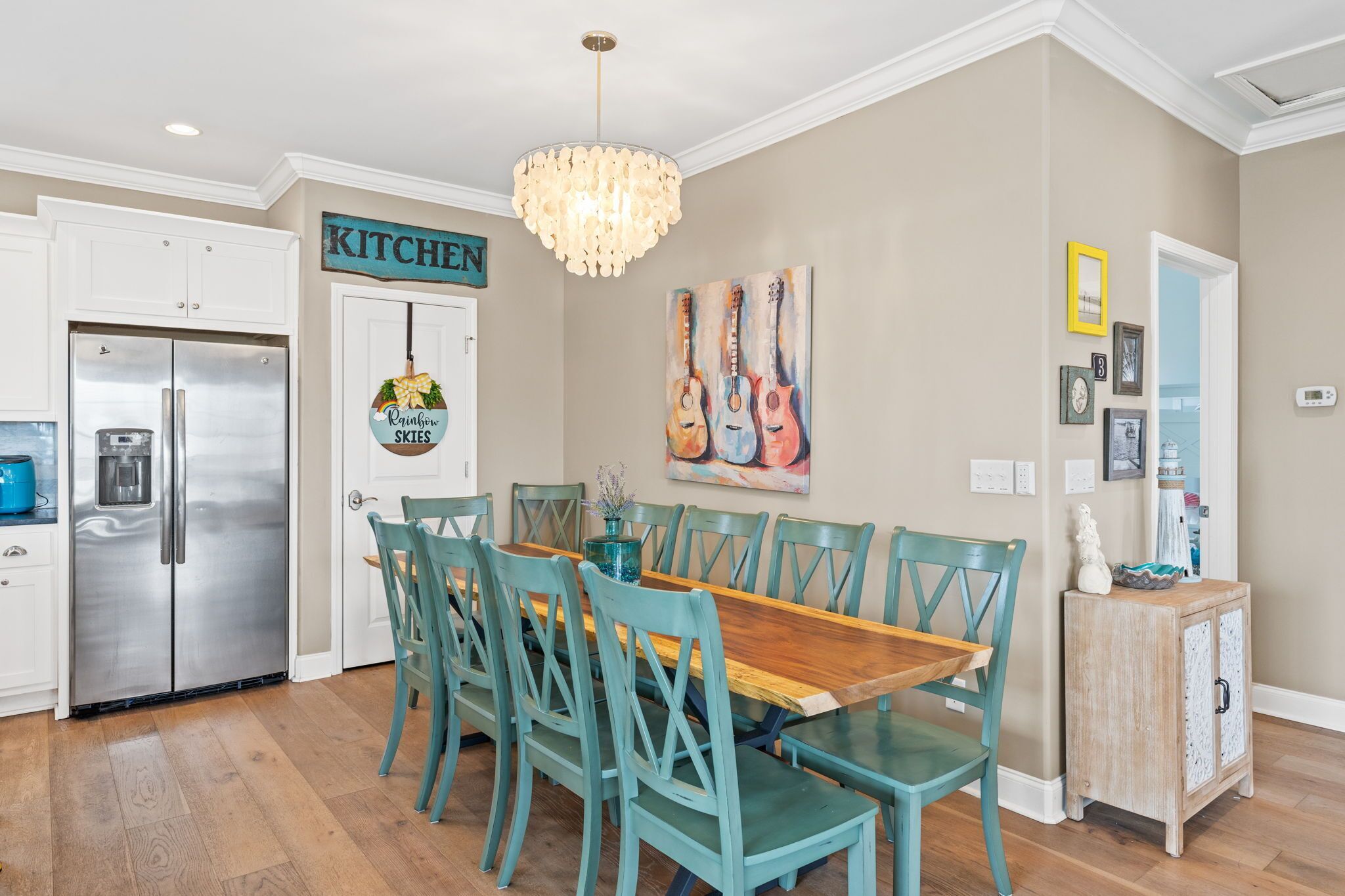 A dining area with teal chairs and a wooden table, a kitchen sign, and a chandelier.