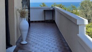 A balcony with a view of the sea, a white vase with dried plants, and a small table. - B&B Villa Alma (San Costanzo)