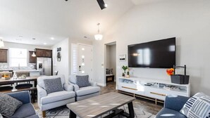 A modern living room with a sofa set, a coffee table, a TV, and a kitchen area with cabinets and appliances. - 3 Bed Single Floor Sleeps w/pool (Washington)