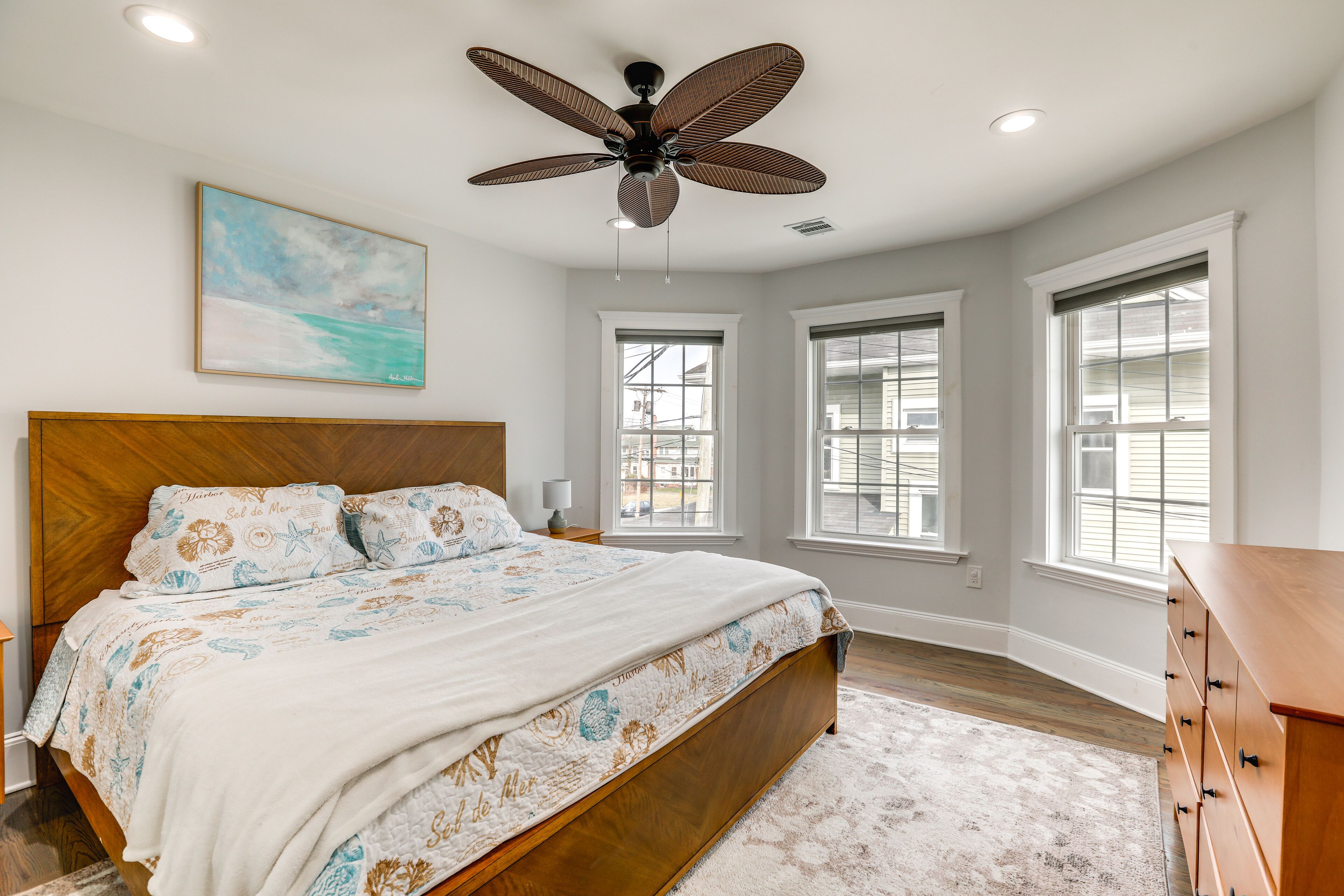 Une chambre avec un lit en bois, un ventilateur de plafond et de grandes fenêtres.