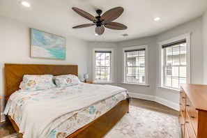 Un dormitorio con cama de madera, ventilador de techo y ventanas amplias.