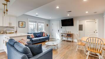 A spacious living room with a blue sofa, a round coffee table, and a dining area with a wooden table and chairs.