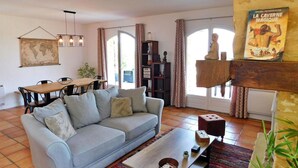 Una sala de estar con un sofá, una mesa de centro y un comedor con una mesa de madera y sillas. Hay una estantería y un mapa del mundo en la pared.