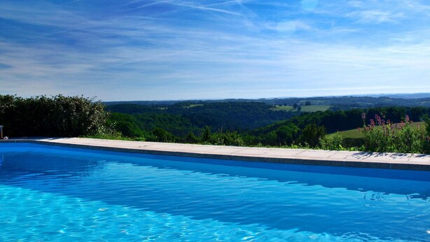Una piscina con vista a un paisaje verde y colinas al fondo.