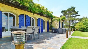 Un patio al aire libre con suelo de piedra, contraventanas azules y mobiliario exterior.