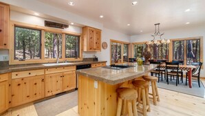 A spacious kitchen with wooden cabinets, a large island with stools, and a dining area with a chandelier.
