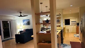 Un salon comprenant un canapé, une table basse et un coin repas avec une table et des chaises. Il y a également une cuisine équipée de placards et d’un réfrigérateur.