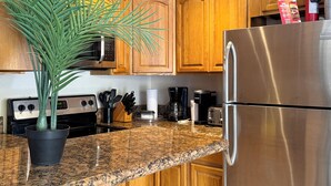 A modern kitchen with wooden cabinets, a granite countertop, a stainless steel refrigerator, a coffee maker, and a potted plant. - ATTENTION: Frequent Island wide power outages likely! Summer/Fall 2026. (Nassau)