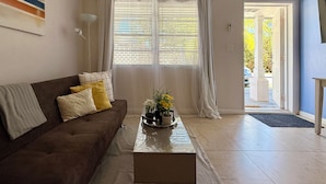 A living room with a brown sofa, a coffee table with a vase of flowers, and a large window with curtains. - ATTENTION: Frequent Island wide power outages likely! Summer/Fall 2026. (Nassau)