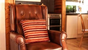 Een bruine leren fauteuil met een gestreept kussen, geplaatst tegen een houten wand in een kamer met een keuken op de achtergrond.