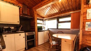Een kleine keuken met houten kastjes, een fornuis en een eethoek met een tafel en stoelen.