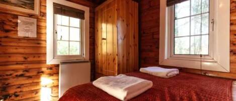 Une pièce de style cabane en bois, comprenant un lit, deux fenêtres et une armoire.