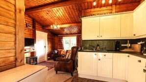 Een gezellig chaletinterieur met houten wanden, een eethoek, een keuken met witte kasten en een open haard.
